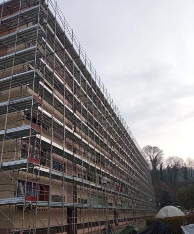 Construction site with a large scaffolded building under a cloudy sky.