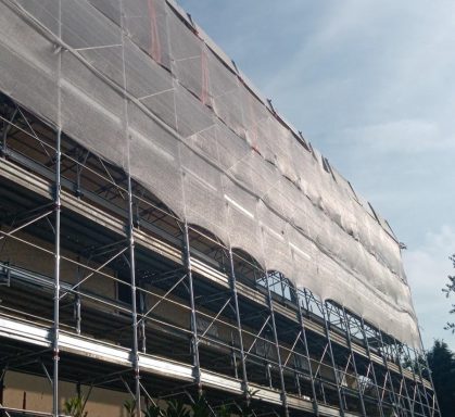 Facciata di un edificio con impalcature e telo di protezione.
