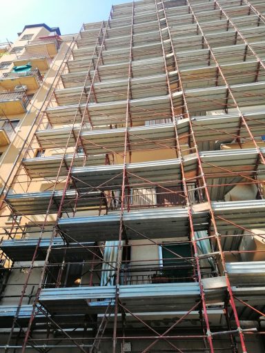 Edificio in costruzione con impalcature metalliche e balconi visibili.